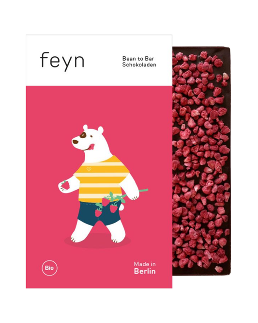 Ein Schokoladenriegel, der teilweise in eine Verpackung eingewickelt ist, die einen weißen Bären in einem gelb gestreiften Hemd zeigt, der Himbeeren auf einem rosa Hintergrund hält. Feyn | Dunkle Schokolade mit Himbeeren ist mit Himbeerstückchen bestreut. Text: Feyn, Bean to Bar Schokoladen, Made in Berlin.