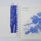 Das „KGA Gartentagebuch | ‚Five Years Diary‘“ in limitierter Auflage der Königlichen Gartenakademie ist aufgeschlagen zu sehen und gibt den Blick frei auf linierte Seiten sowie eine blau illustrierte Januar-Seite mit Cedrus atlantica. Ein botanisches Lesezeichen mit der Aufschrift „Hyacinthus orientalis“ liegt auf der linken Seite; alle Illustrationen sind in Blau auf Weiß gehalten. Dieses als limitierte Auflage gefertigte Tagebuch ist eine einzigartige Bereicherung für die Sammlung jedes Gartenliebhabers.
