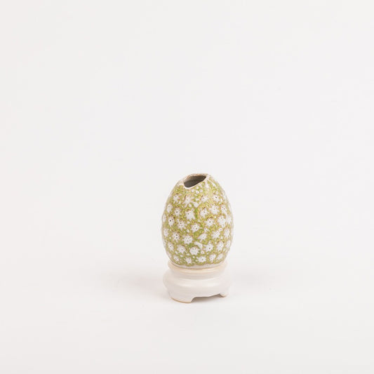 Die Des Pots | Vase Ei-auf-Schale Form klein (H 10 cm, Ø 5,5 cm) von Königliche Gartenakademie ist eine eiförmige, handgemachte Keramikvase mit grün-weißem Blumenmuster, glasiert und auf einer kleinen weißen Schale platziert.