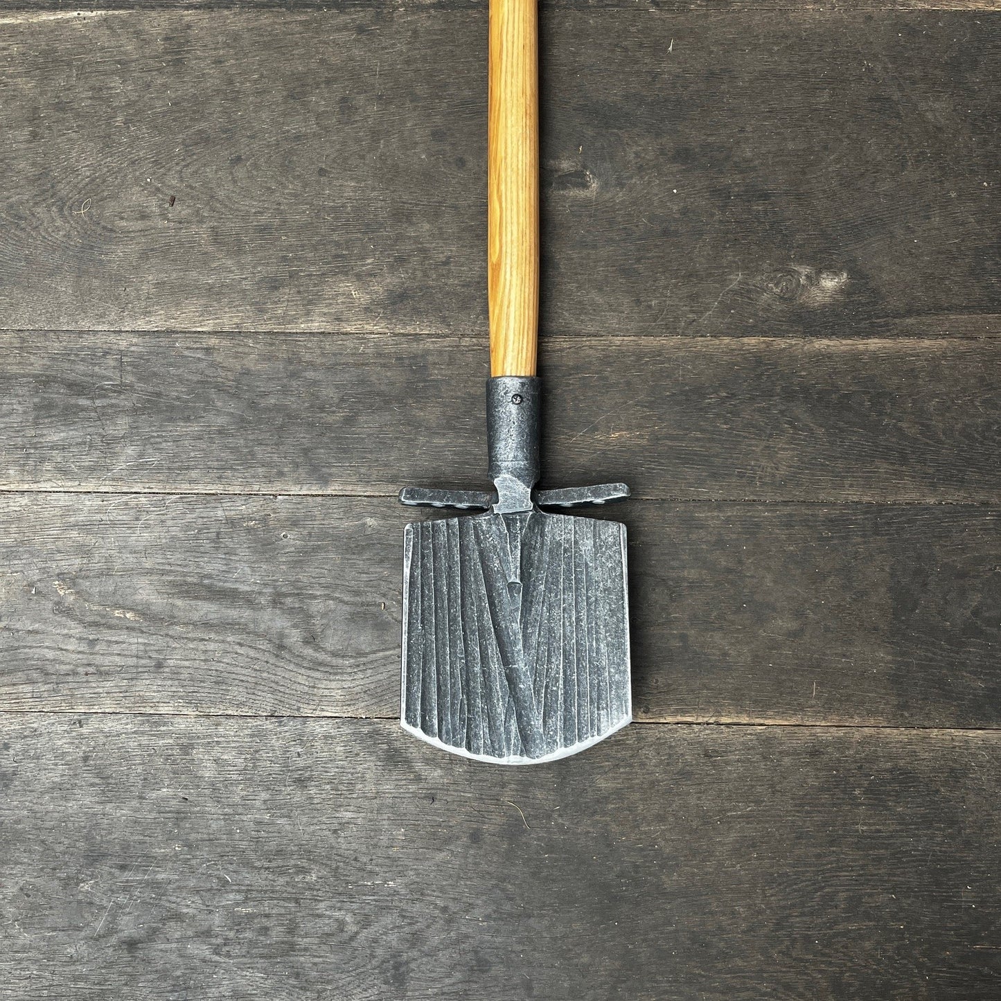 Der Krumpholz Damenspaten 'Elke' 85cm 1589 liegt mit seiner Klinge nach unten und dem Holzgriff nach oben auf dunklem, wettergegerbtem Holzboden - ein vielseitiger Spaten für rückenschonendes Arbeiten.