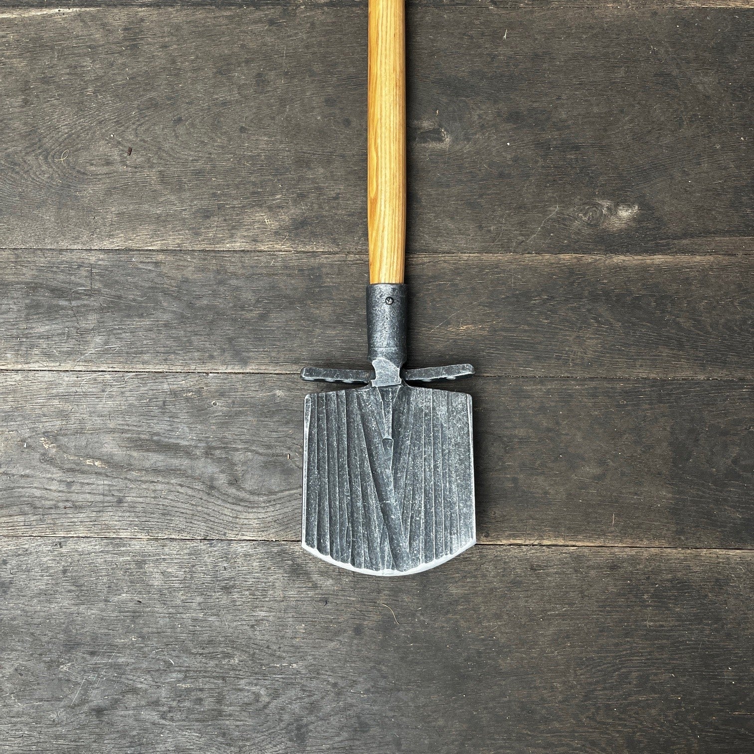 Der Krumpholz Damenspaten 'Elke' 85cm 1589 liegt mit seiner Klinge nach unten und dem Holzgriff nach oben auf dunklem, wettergegerbtem Holzboden - ein vielseitiger Spaten für rückenschonendes Arbeiten.
