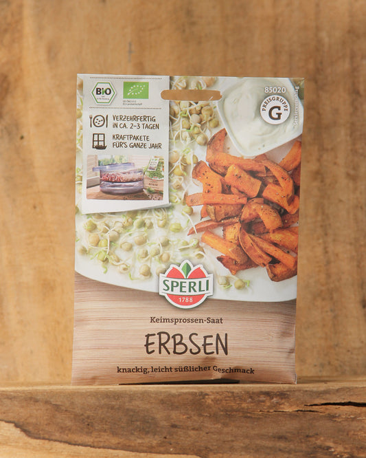 Eine Packung Sperli's Bio Keimsprossen Saatgut 'Erbsen' von Sperli's liegt auf einer Holzplatte, die Verpackung zeigt frische grüne Erbsensprossen und geröstete Süßkartoffelscheiben auf einem weißen Teller.