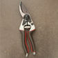 Ein Paar Felco 8 ELITE Gartenscheren von Felco mit braunen ergonomischen Griffen und einer silbernen Klinge ruht auf einer strukturierten braunen Oberfläche.