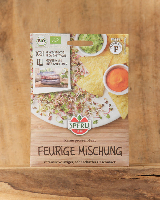 Die Saatgutpackung Bio Keimsprossen Saatgut 'Feurige Mischung' von Sperli zeigt würzige Keimsprossen, Tortilla-Chips und Dips auf einem Holztisch. Der Text hebt Bio-Keimsprossen und eine würzige Mischung für selbst gezogene Sprossen hervor. Marke: Sperli's.