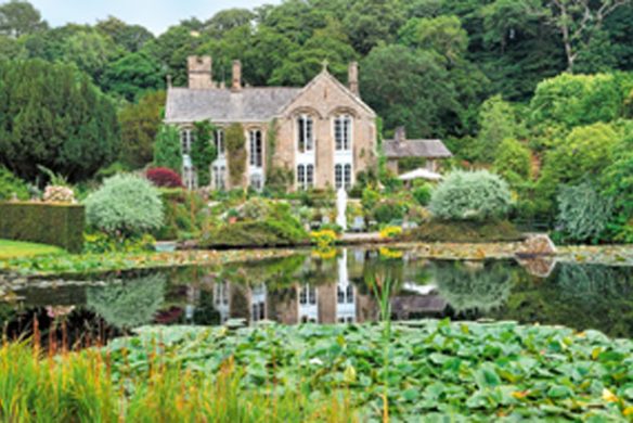 Umgeben von üppigen Gärten, die von "Gärtnern wie Gott in England" aus dem Callwey Verlag inspiriert sind, spiegelt sich ein steinernes Herrenhaus mit hohen Fenstern in einem Seerosenteich, der von dichten Bäumen umrahmt wird.
