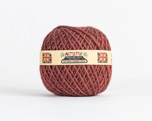 Ein Knäuel brauner Gartenschnur mit der Aufschrift „Nutscene | Heritage Jutegarn in Henna 130 m“ von Nutscene Twines Ltd weist ein beiges Etikett mit Union-Jack-Flaggen und den Schriftzügen „Nutscene“ und „The Ideal Garden Twine“ auf, die sich vor einem schlichten weißen Hintergrund abheben.