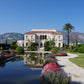 Eine rosafarbene Villa spiegelt sich im Gartenpool der Königlichen Gartenakademie während der Veranstaltung am Di., 16.3.2027 | 14.30 – 15.30 Uhr AFTERNOON TEA – Gartenreise durch Frankreich, umgeben von gepflegten Beeten und Wegen.