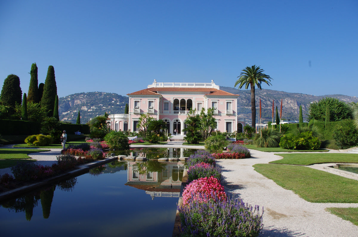 Eine rosafarbene Villa spiegelt sich im Gartenpool der Königlichen Gartenakademie während der Veranstaltung am Di., 16.3.2027 | 14.30 – 15.30 Uhr AFTERNOON TEA – Gartenreise durch Frankreich, umgeben von gepflegten Beeten und Wegen.