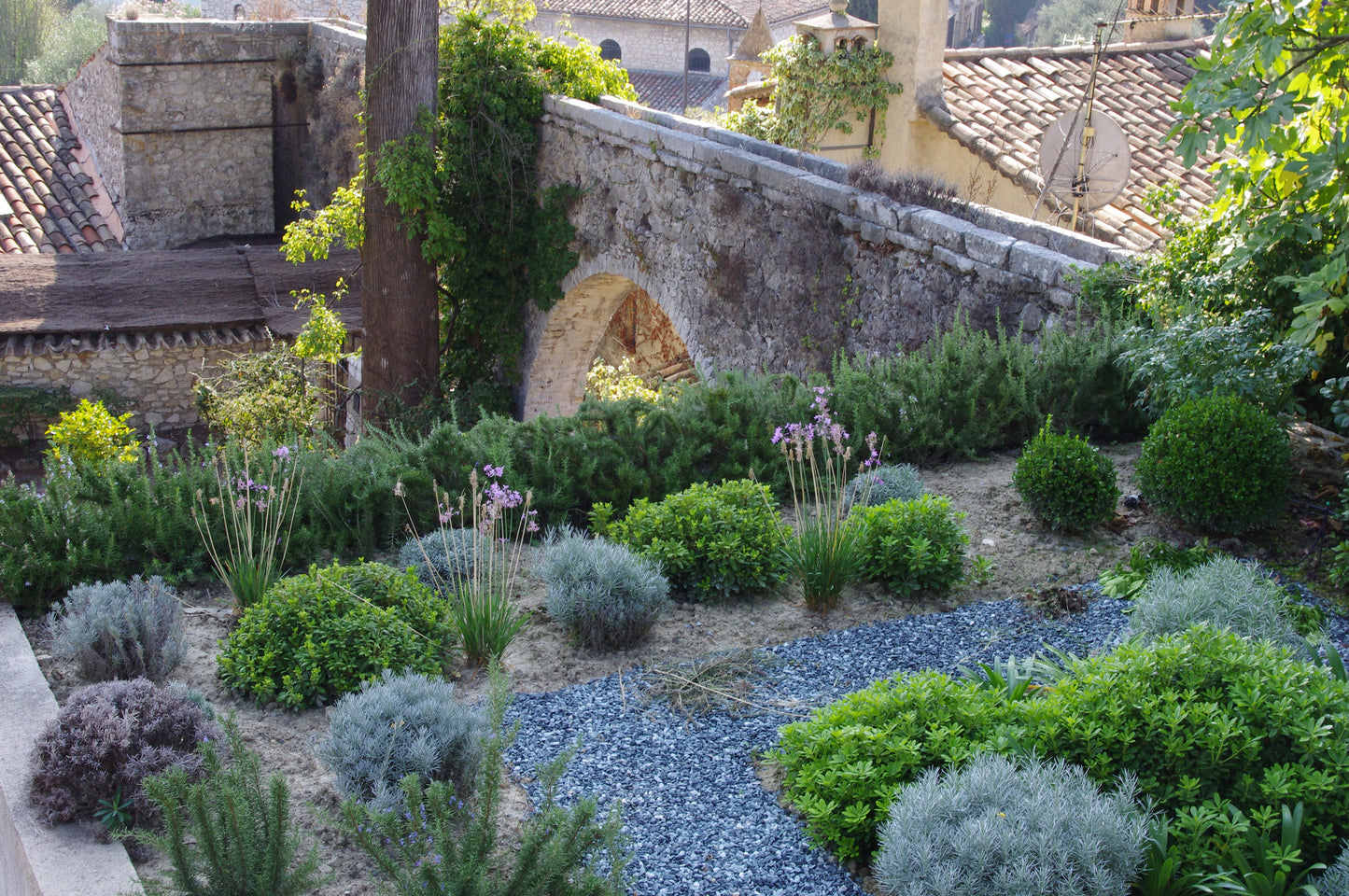 Erleben Sie einen üppigen mediterranen Garten beim WORKSHOP "Kräuter pflanzen und pflegen" der Königlichen Gartenakademie am Mi. 01.04.2026, 10-11:30 Uhr, umgeben von grünen Sträuchern, Lavendel und blühenden Pflanzen an reizvollen Steinwegen und rustikalen Mauern.
