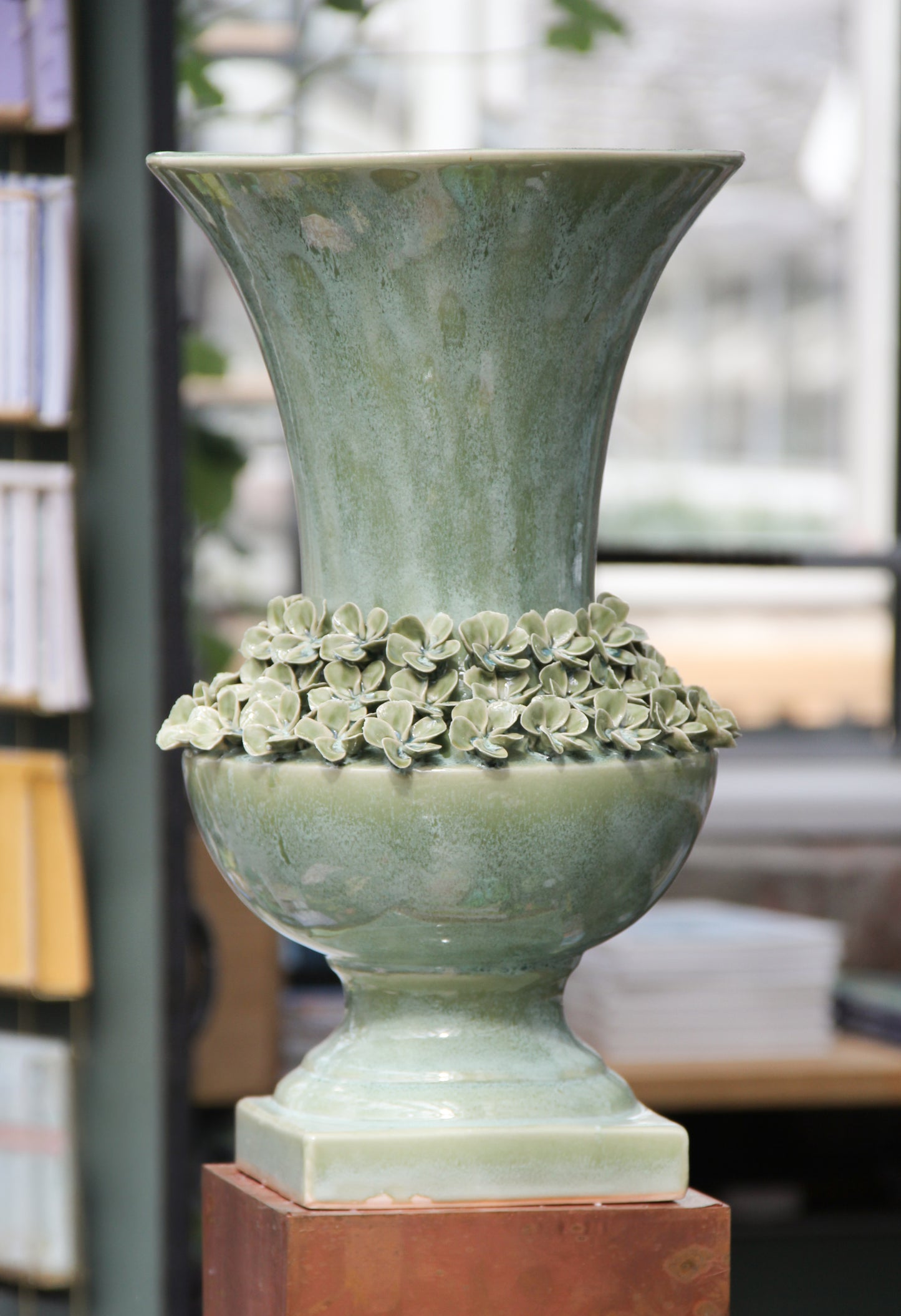 Die „Amphore in Grün aus Steingut, 25 x 41,5 cm“ von Werner Voß, mit ausgestellter Kante und einem Keramik-Blumenring in der Mitte, steht im Innenraum in der Nähe von Regalen und Büchern und verleiht dem Raum einen Hauch mediterraner Dekoration.