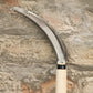 Eine Niwaki „Herbaceous Sickle“ Nokogama Reissichel aus Kohlenstoffstahl (32 cm) mit gezahnter Klinge und einem leichten Holzgriff lehnt an einer strukturierten Steinmauer – ein unverzichtbares Gartenwerkzeug von Niwaki für präzisen Schnitt.