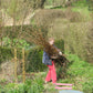 Eine Person trägt ein großes Bündel abgeschnittener Äste durch den Garten für den Di., 9.3.2027 | 10.00 – 12.00 Uhr WORKSHOP Frühlingsfit: Wie bereite ich den Garten auf die neue Saison vor?.