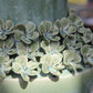 Nahaufnahme der „Amphore in Grün aus Steingut, 25 x 41,5 cm“ von Werner Voß – eine Keramikvase mit sorgfältig modellierten Blumenmotiven, deren hellgrüne Blütenblätter und blaue Akzente kunstvoll um den Sockel herum angeordnet sind und einen eleganten Hauch mediterraner Atmosphäre vermitteln.