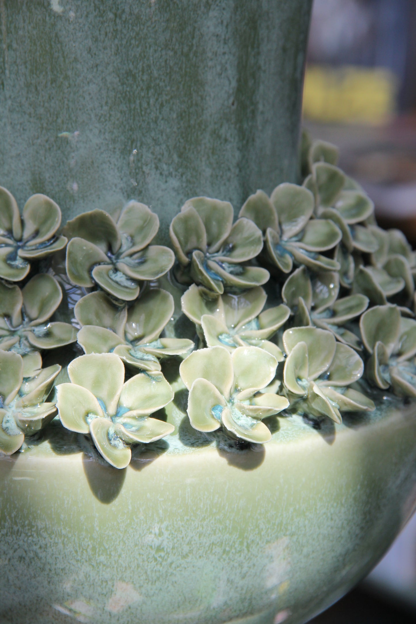 Nahaufnahme der „Amphore in Grün aus Steingut, 25 x 41,5 cm“ von Werner Voß – eine Keramikvase mit sorgfältig modellierten Blumenmotiven, deren hellgrüne Blütenblätter und blaue Akzente kunstvoll um den Sockel herum angeordnet sind und einen eleganten Hauch mediterraner Atmosphäre vermitteln.
