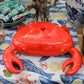 Eine leuchtend rote „Summer Bliss Crab“-Krabben-Schale von Costa Nova aus Keramik, die in Form einer Krabbe mit abnehmbarem Deckel gestaltet ist, steht auf einer Tischdecke mit maritimem Muster, umgeben von weiteren Dekorationselementen zum Thema Meeresfrüchte.