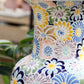 Eine Nahaufnahme der Vase „Des Pots | Bunte Vase aus Keramik mit Blumenmuster H 20 T 10“ von Des Pots, die sich durch farbenfrohe, handgemalte Blumenmuster in Blau-, Gelb-, Grün- und Pastelltönen vor einem verschwommenen Innenraumhintergrund auszeichnet. Diese glasierte Keramikvase ist 20 cm hoch und besticht durch exquisite Handwerkskunst.