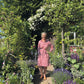 Eine Frau steht auf einem Ziegelweg in einem üppigen Garten während eines Halbtageskurses Grundlagen der Gartengestaltung am Samstag, 27.2.2027 | 10.00 – 13.00 Uhr, umgeben von blühenden Blumen und Sträuchern.