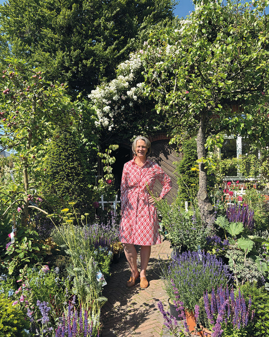 Eine Frau in einem rot-weißen Kleid lächelt auf einem sonnigen Gartenweg - ein inspirierender Anblick für alle Garteninteressierten beim HALBTAGESKURS "Der Garten als Lebensraum NEU" der Königlichen Gartenakademie am Mi. 18.02.2026, 09.30-12.30.