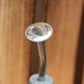 Eine Nahaufnahme der „Esschert Gießbrause Ball Grau L“, einer Gießkanne aus Metall mit kleinen Löchern für eine wassersparende und gezielte Pflanzenbewässerung, die an einem weißen Griff befestigt ist und vor einem Holzhintergrund steht.