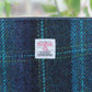 Handgewebte Tasche mit Reißverschluss | „Berneray“ Medium, türkisblau mit türkisfarbenem Karomuster (23 x 11 cm) von Glen Appin, präsentiert vor sattem Grün und einer verschwommenen Naturlandschaft – ein echter Blickfang, der die kunstvolle Handarbeit dieses einzigartigen Stücks unterstreicht.