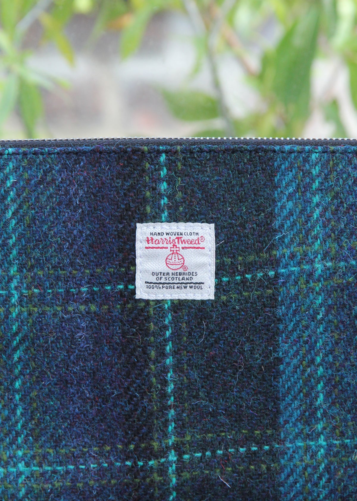 Handgewebte Tasche mit Reißverschluss | „Berneray“ Medium, türkisblau mit türkisfarbenem Karomuster (23 x 11 cm) von Glen Appin, präsentiert vor sattem Grün und einer verschwommenen Naturlandschaft – ein echter Blickfang, der die kunstvolle Handarbeit dieses einzigartigen Stücks unterstreicht.