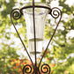 Ein Regenmesser mit Glas | Für den Gartenliebhaber, inkl. filigranem Universalstab, H 125 cm, von Hirsch, teilweise mit Wasser gefüllt, steht aufrecht in seinem dekorativen Metallständer, im Hintergrund ist sanft verschwommenes grünes und rotes Laub zu sehen.