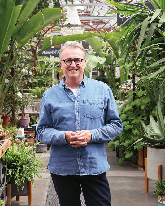 Horst Mager, im hellen Jeanshemd, steht lächelnd zwischen üppigen Pflanzen in einem sonnigen Gewächshaus - bereit, seine besten Tipps bei der Königlichen Gartenakademie HALBTAGESKURS "Das Gartenjahr - Monat für Monat", Fr. 13.03.2026, 13.00-16.00 Uhr, zu geben.