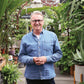 Horst Mager, im Jeanshemd und mit Brille, steht inmitten üppiger Gewächshauspflanzen - Ihr Guide für den "Fr. 15.05.2026 | 13.00-16.00 HALBTAGESKURS Das Gartenjahr-Monat für Monat" in der Königlichen Gartenakademie.