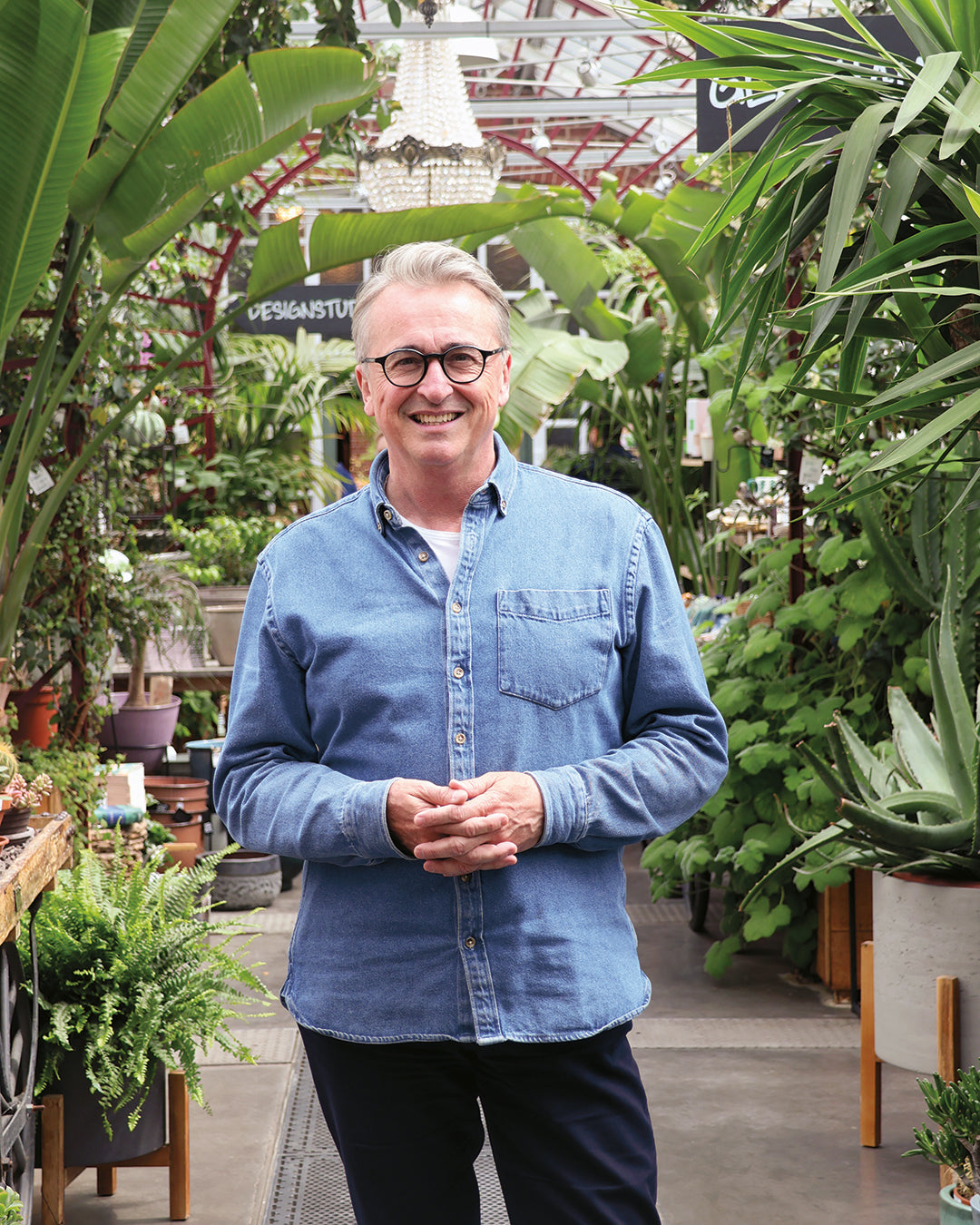 Horst Mager, im Jeanshemd und mit Brille, steht inmitten üppiger Gewächshauspflanzen - Ihr Guide für den "Fr. 15.05.2026 | 13.00-16.00 HALBTAGESKURS Das Gartenjahr-Monat für Monat" in der Königlichen Gartenakademie.