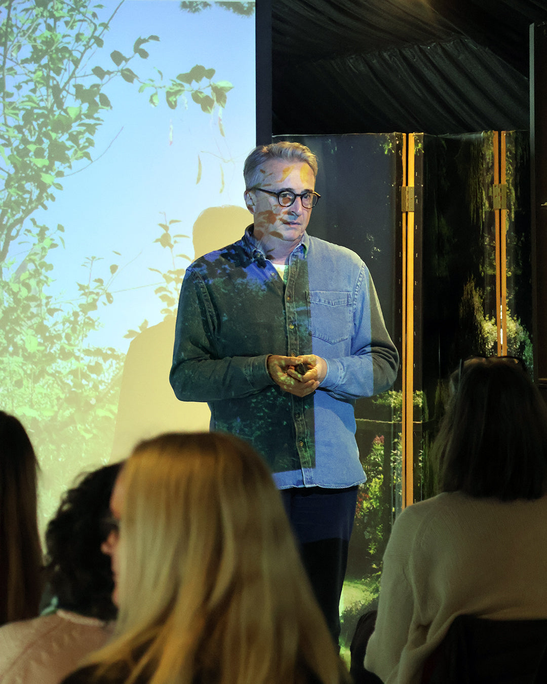 Horst Mager leitet den Halbtageskurs "Das Gartenjahr-Monat für Monat" der Königlichen Gartenakademie am Fr. 15.05.2026, 13-16h, und spricht vor einem aufmerksamen Publikum, während hinter ihm eine Naturszene projiziert wird.
