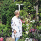 Eine Frau steht in einem üppigen Garten mit professioneller Beetgestaltung inmitten von Topfblumen und Grünpflanzen für Mi., den 10.3. - Do., 11.3.2027 | 10.00 – 16.30 Uhr ZWEITÄGIGER MEISTERKURS Gestalten Sie Ihr eigenes Beet.