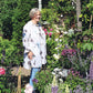 Eine ältere Frau lächelt in einem lebendigen Garten und bewundert ihr Blumenbeet, das sie beim "ZWEI-TAGES-MASTERCLASS Gestalten Sie Ihr eigenes Beet" der Königlichen Gartenakademie (Mi. 28.10 - Do. 29.10.2026 | 10:00-16:30) angelegt hat. Das Sonnenlicht erhellt die fröhliche Szene.