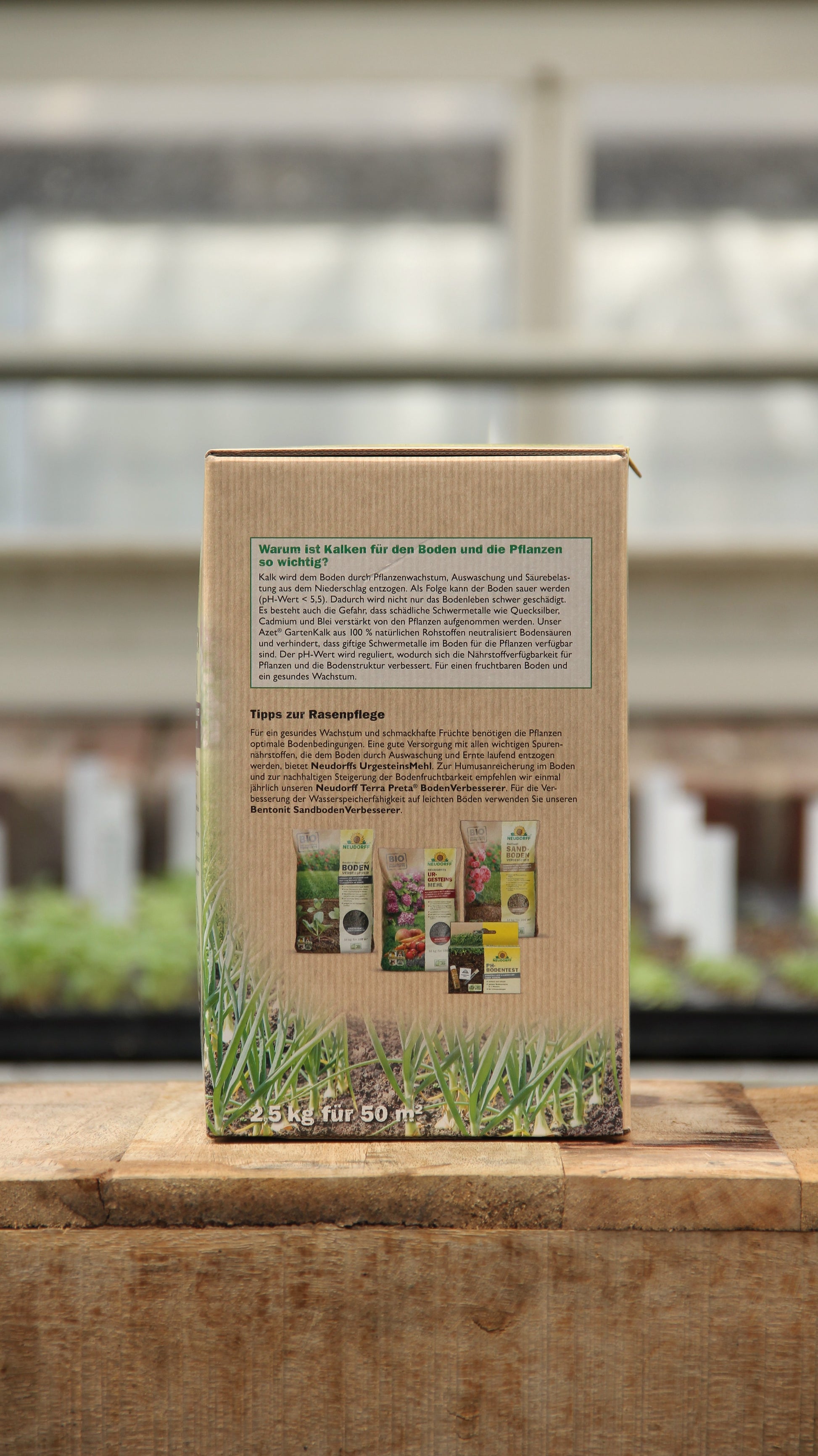 Eine 2,5 kg Kiste Neudorff Gartenkalk Bodenverbesserer aus natürlichen Rohstoffen steht auf Holz; das deutsche Etikett und die Gewächshauskeimlinge weisen auf die Verwendung zur Regulierung des pH-Wertes im Boden hin.