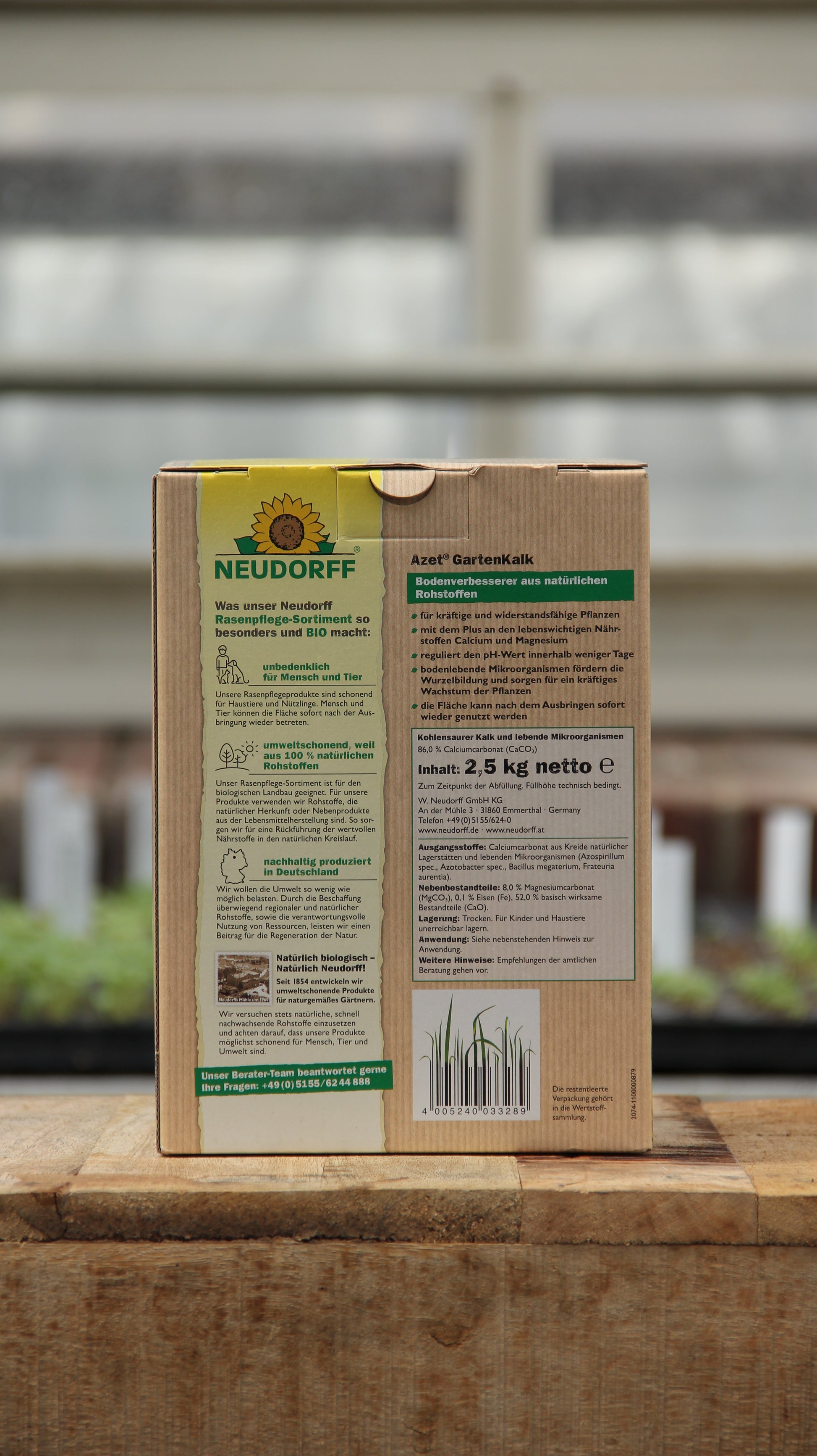 Eine 2,5-kg-Packung Neudorff Gartenkalk Bodenverbesserer aus natürlichen Rohstoffen steht auf Holz, mit deutschen Infos und grün-gelben Akzenten. Unscharfe Zimmerpflanzen und ein Fenster im Hintergrund - ideal zur pH-Wert-Regulierung.
