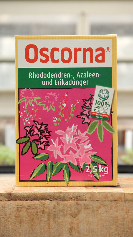 Eine 2,5-kg-Packung Oscorna Rhododendren-, Azaleen- und Erikadünger Naturdünger, ein organischer Dünger für Rhododendren, Azaleen und Heidepflanzen; hergestellt aus 100 % natürlichen Zutaten mit rosafarbenen Blumenmotiven auf der Verpackung.