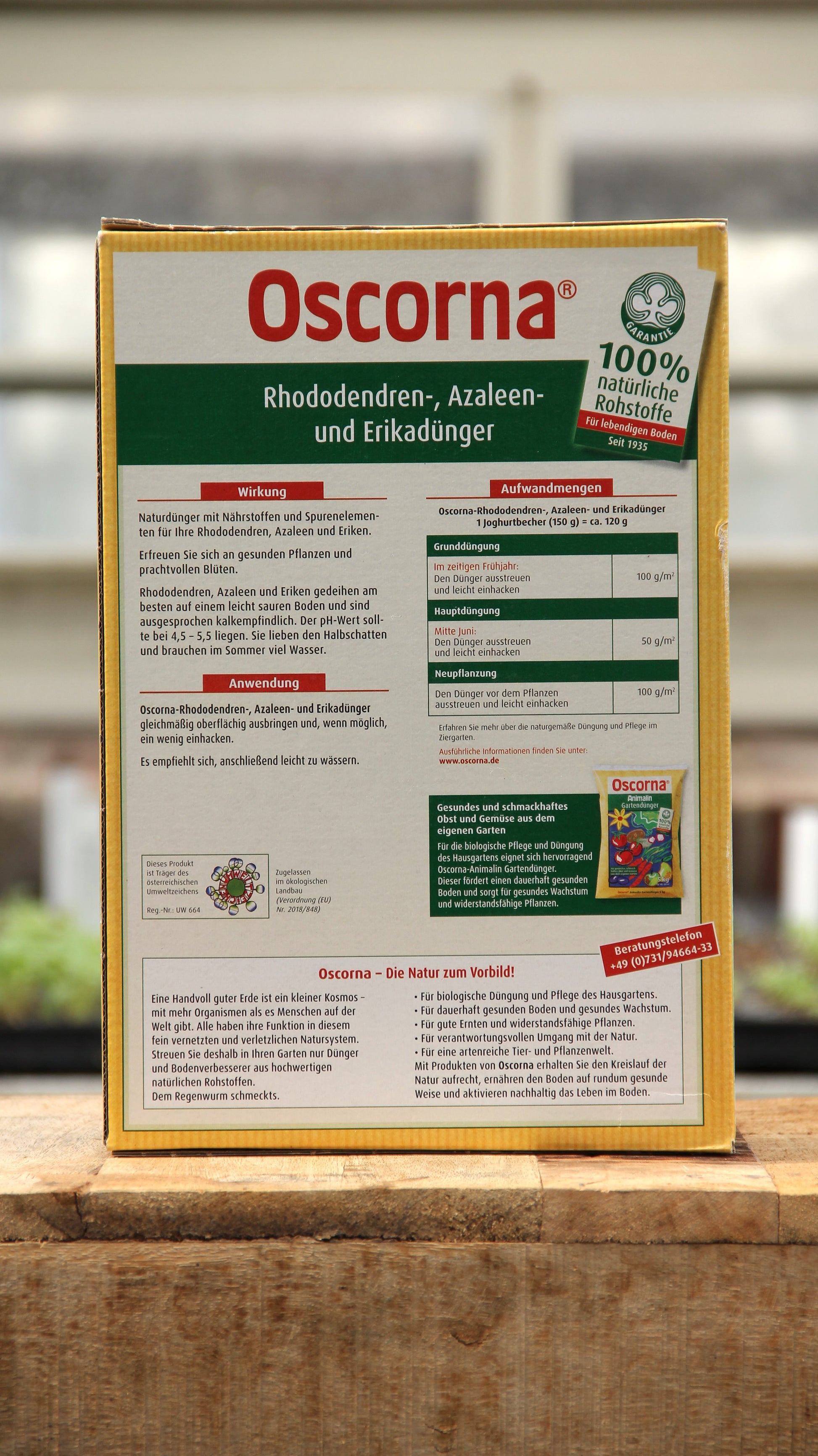 Eine 2,5 kg Kiste Oscorna Rhododendren-, Azaleen- und Erikadünger Naturdünger steht auf einer Holzunterlage mit einer ausführlichen deutschen Anleitung. Dieser organische Dünger von Oscorna unterstützt ein gesundes, kräftiges Wachstum von Rhododendren und Azaleen.
