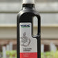Eine schwarze 1L-Flasche Wuxal | Calciumdünger für Obstbäume, Gemüse -& Zierpflanzen mit weißem Deckel und Griff steht auf Holz. Das Etikett zeigt eine Tomatenpflanze und einen deutschen Text. Im Hintergrund erscheinen verschwommene Grünflächen und helles Licht.