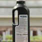 Eine schwarze 1-Liter-Kunststoffflasche von Wuxal-Kalkdünger für Obstbäume, Gemüse und Zierpflanzen mit weißem Deckel, Griff und Etikett mit Produktinformationen und Warnhinweisen steht auf einer Holzfläche mit unscharfem Hintergrund.