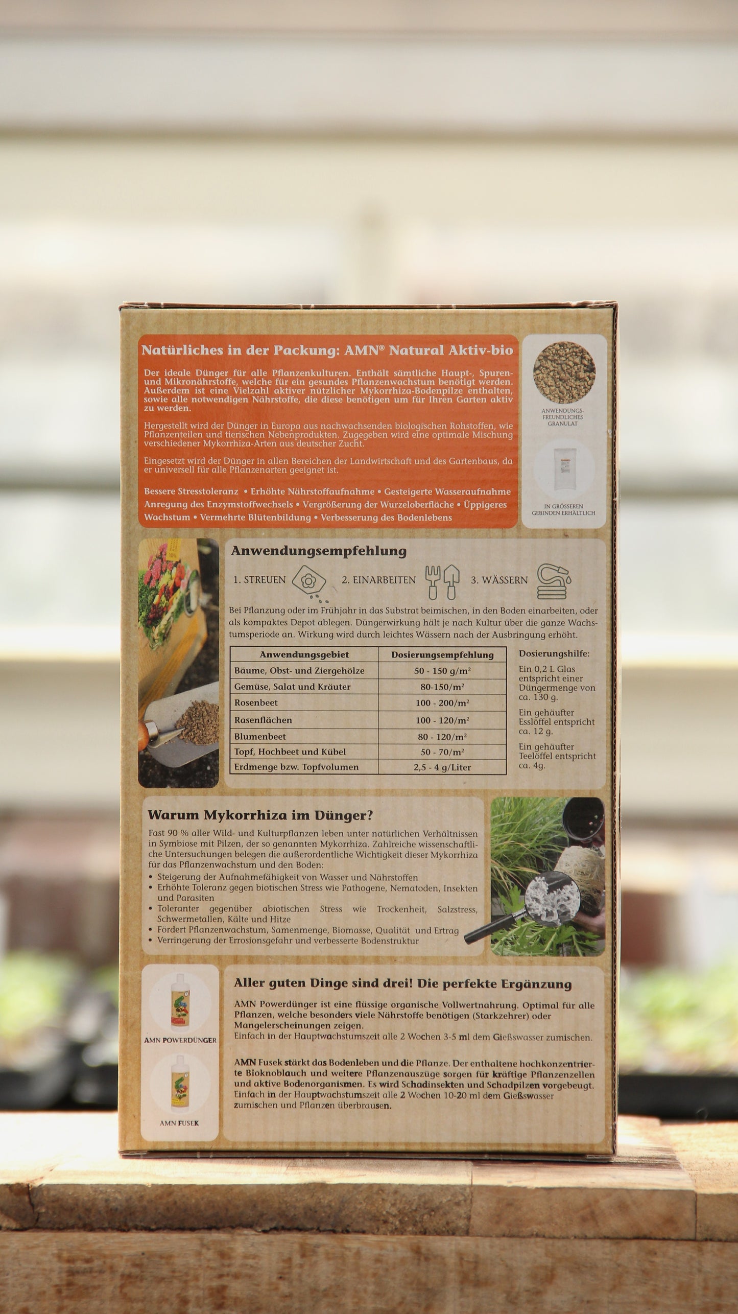 Auf der Rückseite der AMN | 'Natural Aktiv bio' 1,5 kg Schachtel finden Sie deutsche Anweisungen, Vorteile und Anwendungstipps für diesen organischen Dünger. Auf der Verpackung sind Pflanzen, Blumen und Gefäße neben dem AMN-Markennamen abgebildet.