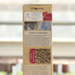 Eine aufrecht stehende Pappschachtel von AMN | 'Natural Aktiv bio' 1,5 kg zeigt einen deutschen Text über Tradition und Innovation, ein altes Foto, ein Fenster mit getrockneten braunen Pellets und verschwommene Pflanzschalen im Hintergrund.