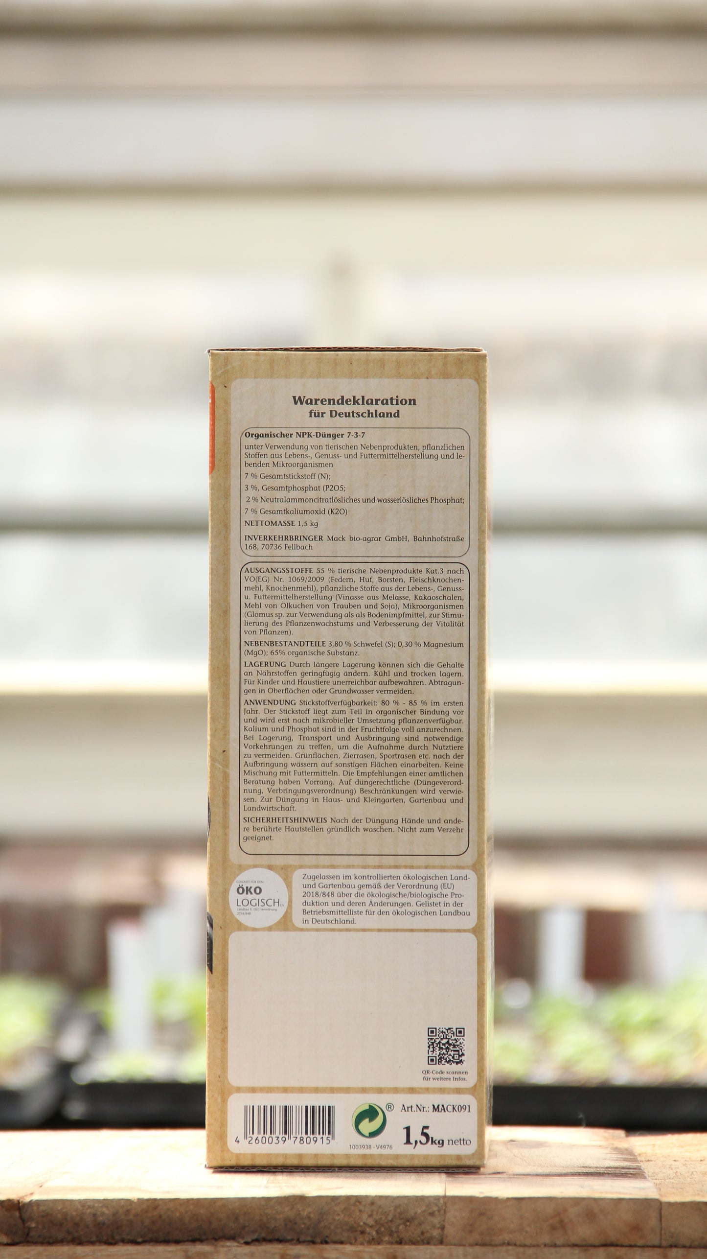 Eine rechteckige Schachtel von AMN "Natural Aktiv bio" 1,5 kg steht aufrecht im Freien; auf der Rückseite ist ein deutscher Text mit Inhaltsstoffen wie Bodenpilze und anderen Produktinformationen zu lesen, im Hintergrund sind Sonnenlicht und unscharfe Pflanzen zu sehen.