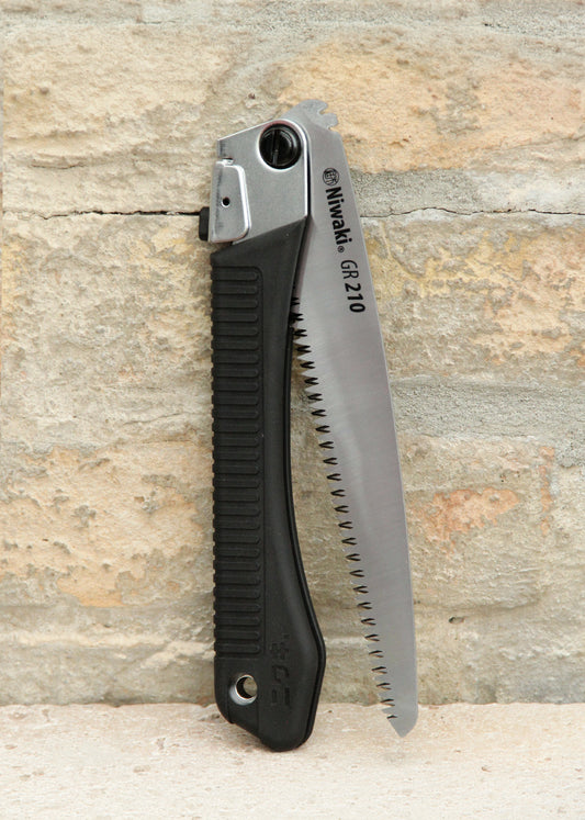 Die Niwaki | „GR 210 Folding Saw“ Klappsäge mit schwarzem, strukturiertem Griff und teilweise freiliegendem silbernem Sägeblatt steht aufrecht vor einer beigen Backsteinmauer – ein ideales Werkzeug von Niwaki für präzise Schnitte in jeder Außenumgebung.
