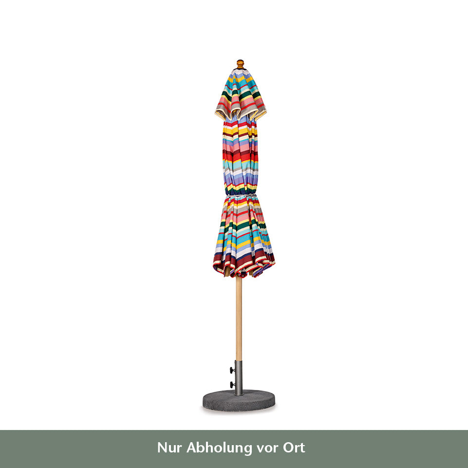 Ein geschlossener Weishäupl Sonnenschirm 'Klassiker Multicolor' Ø 300 cm mit bunten Streifen steht auf einem runden Steinsockel. Darunter steht ein deutscher Text: "Nur Abholung vor Ort".