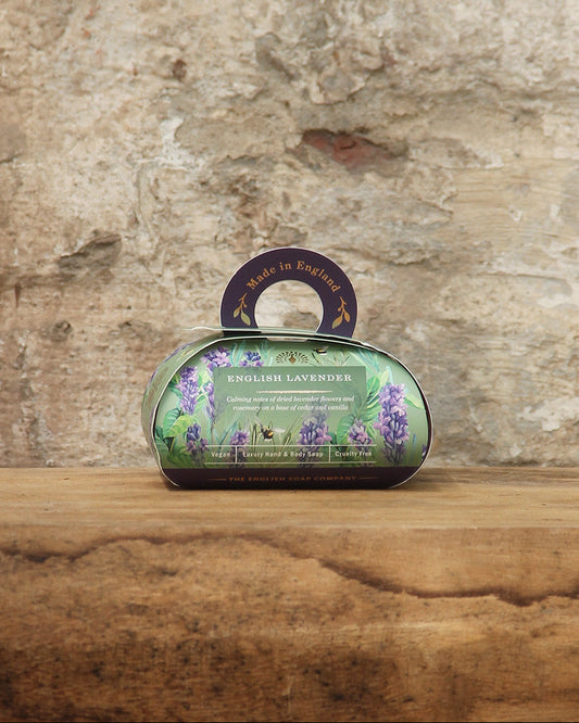 Eine Tafel The English Soap Company ESC 'English Lavender' frisch duftende pflanzliche Handseife in Geschenkbox ruht auf Holz vor einer rustikalen Steinmauer und erinnert an traditionelle Englische Lavendelseife und plastikfreie Verpackung.