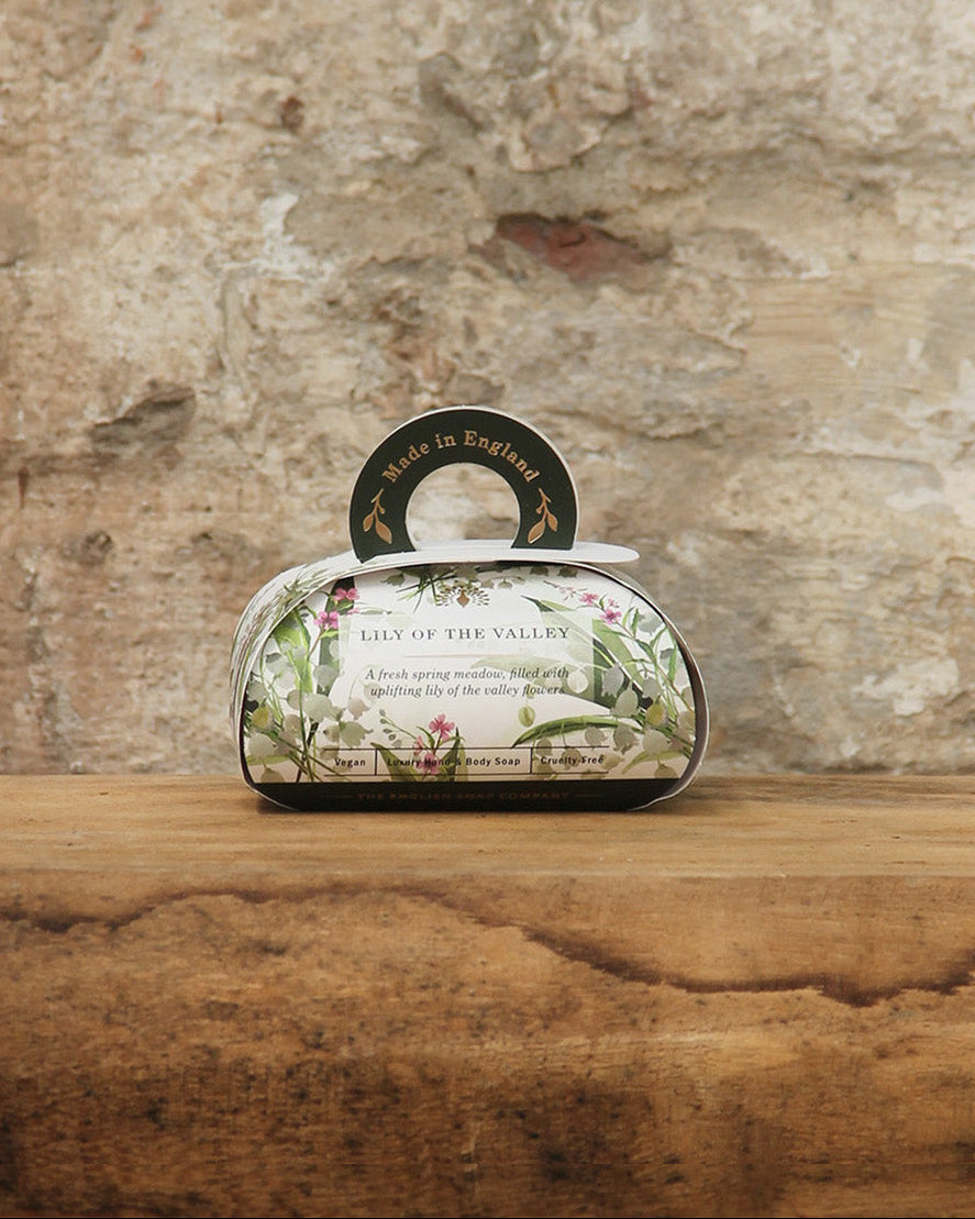 Eine dekorative Box von ESC | 'Lily of the Valley' Pflanzliche Handseife von The English Soap Company mit Maiglöckchenduft steht auf rustikalem Holz vor einer Steinwand - floral verziert und perfekt als Geschenkbox für pflanzliche Luxusseife.