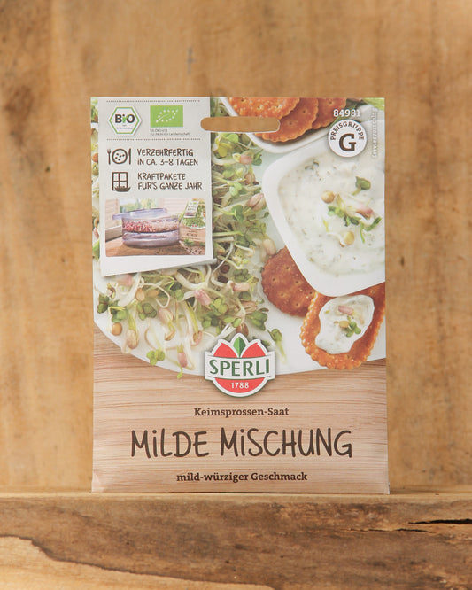 Packung von Sperli's | Bio Keimsprossen Saatgut 'Milde Mischung' mit Bildern von frischen Sprossen und Gerichten auf der Vorderseite. Mit Bio-Keimsprossen-Zertifizierung, deutschem Text und Holzuntergrund. Marke: Sperli's.