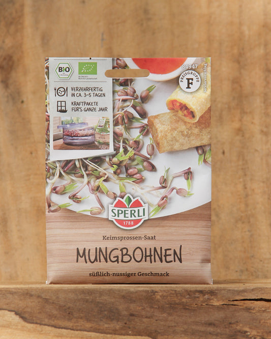 Eine Packung Sperli's Bio Keimsprossen Saatgut 'Mungbohnen' wird auf Holz präsentiert, mit der Marke Sperli's, Bildern von Mungbohnensprossen, einem Bio-Etikett, Servierideen und einem deutschen Text über diese Bio-Keimsprossen.