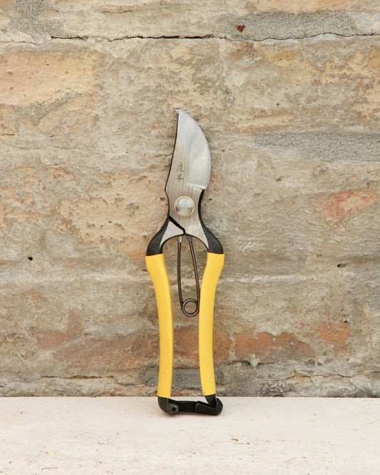 Ein Paar Niwaki | 'Higurashi GR Secateurs' Gartenschere von Niwaki mit gelben und schwarzen Griffen steht aufrecht vor einer strukturierten hellbraunen Steinwand.