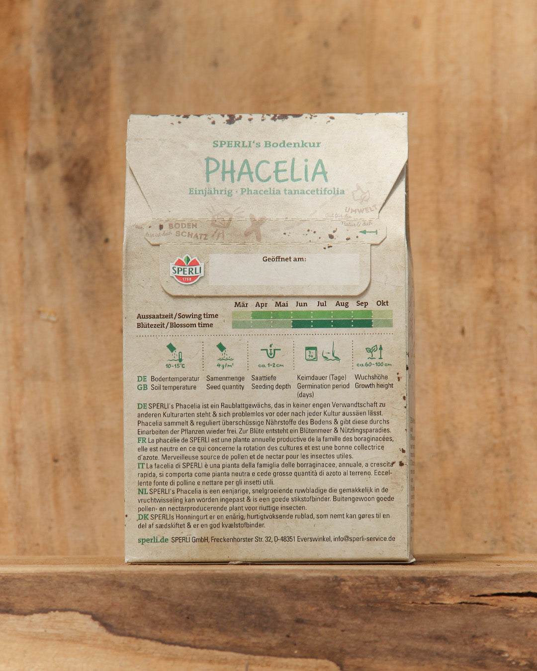 Eine 350 g-Packung Sperli's | Bodenkur 'Phacelia' Gründünger steht aufrecht auf Holz, mit deutscher Aussaat-/Pflegeanleitung, hilfreichen Piktogrammen und einem Kalender zur optimalen Verwendung als Gründüngung zur Bodenverbesserung.