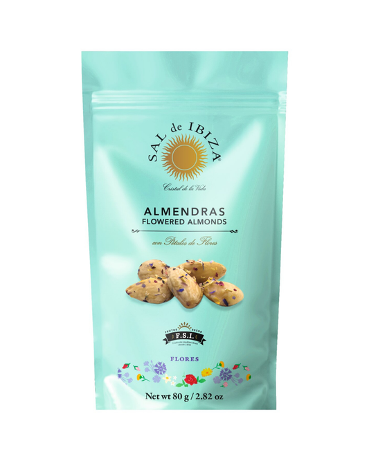 Ein türkisfarbener, wiederverschließbarer 80-g-Beutel von Viani | „Almendras Flores“ – Mandeln mit Blütensalz, verziert mit Mandeln und Blütenblättern, einem Sonnenlogo und floralen Akzenten.